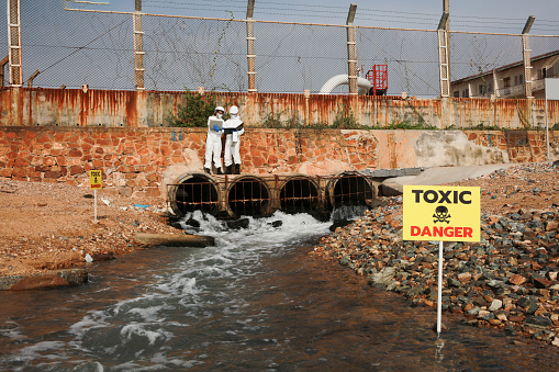 Scientist or biologist wearing protective uniforms analyze the waste water flow to the sea